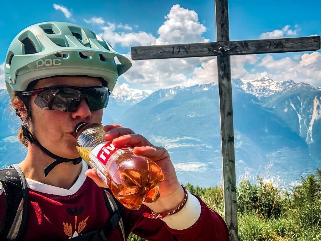 Couchflucht Sabrina Bechtold trinkt am Gipfelkreuz - Pause vom Mountainbiken