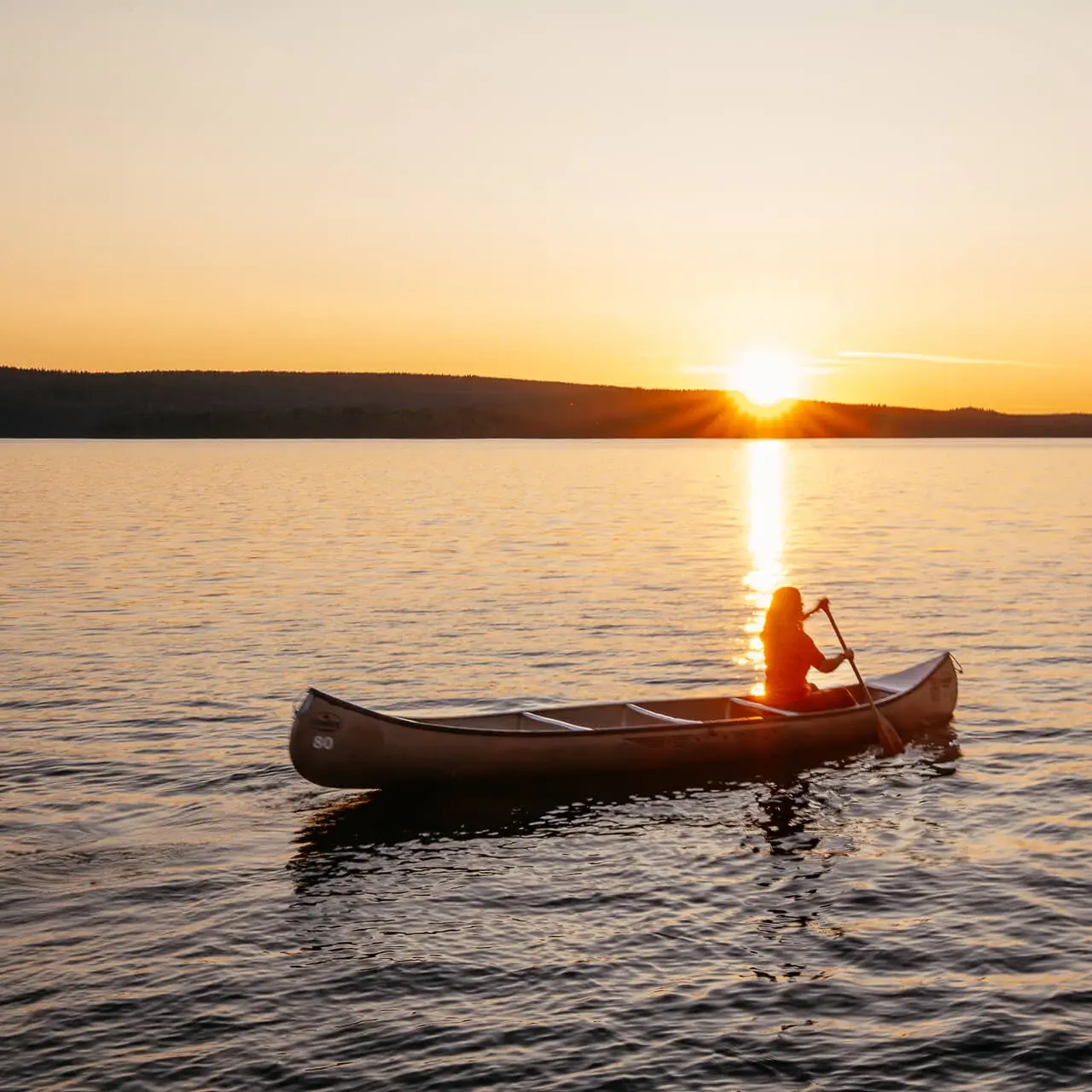 Couchflucht paddelt mit dem Kanu im Sonnenuntergang bei der Kanutour in Schweden.